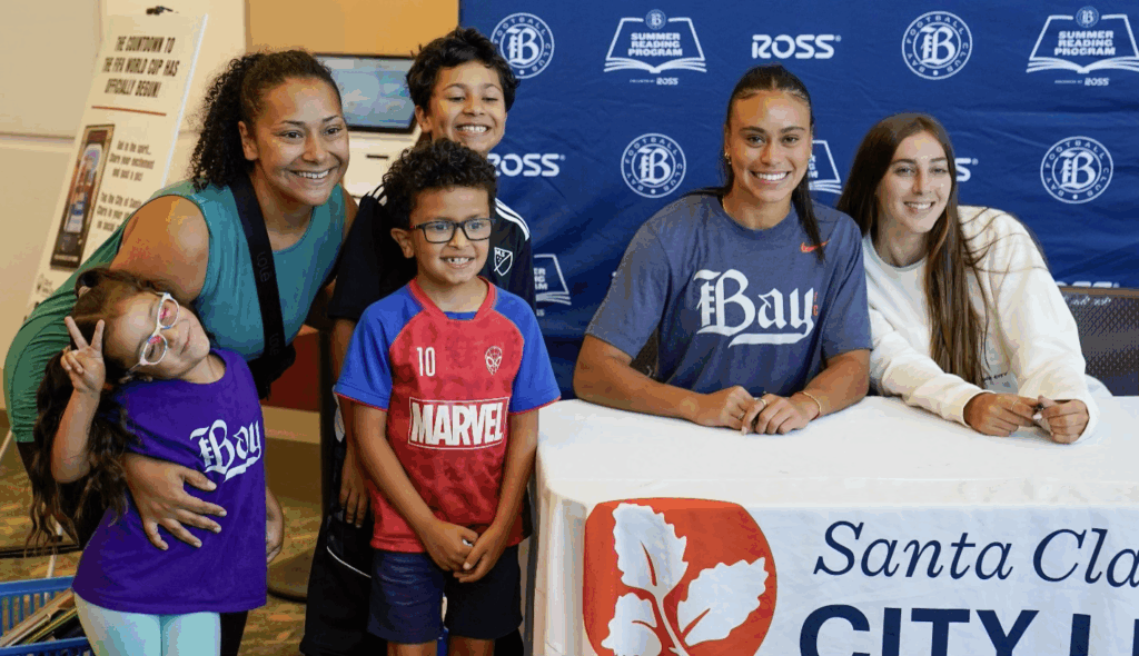 Two Bay FC players and a family at the Summer Adventure storytime.